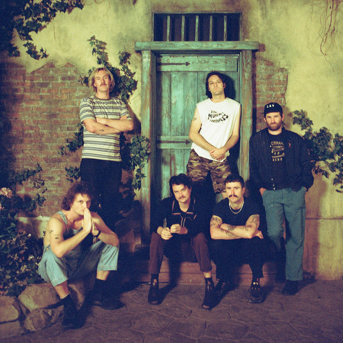 King Gizzard band members posing in front of an old houses wall